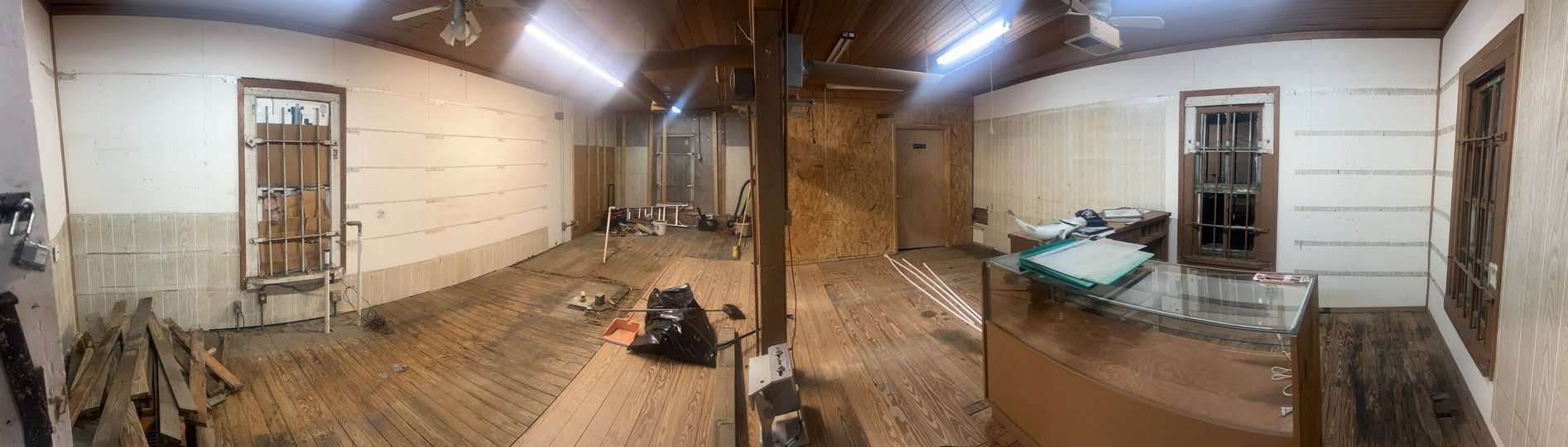 Panoramic view of the Falls Lake Outpost interior during renovation, with bare wood floors and an empty display case